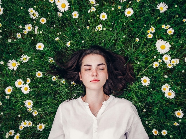Красивая девушка лежит на зеленой траве с ромашками