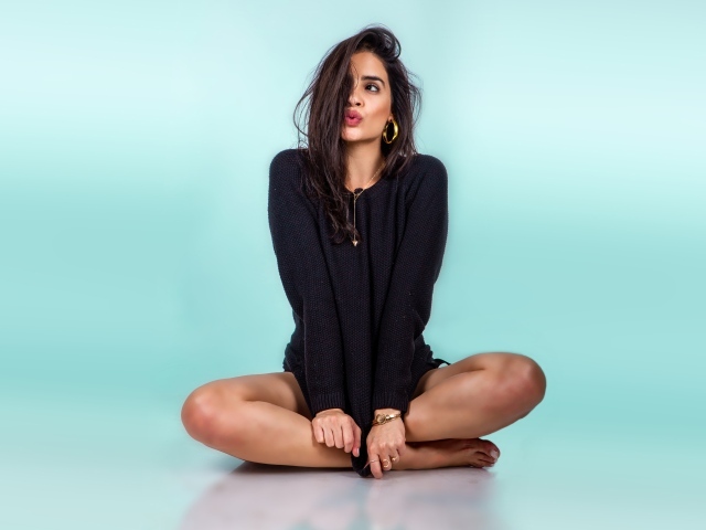 Красивая девушка сидит в черном свитере на голубом фоне