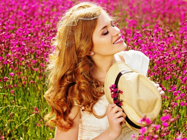 Красивая девушка с шляпой в руках на поле с розовыми цветами