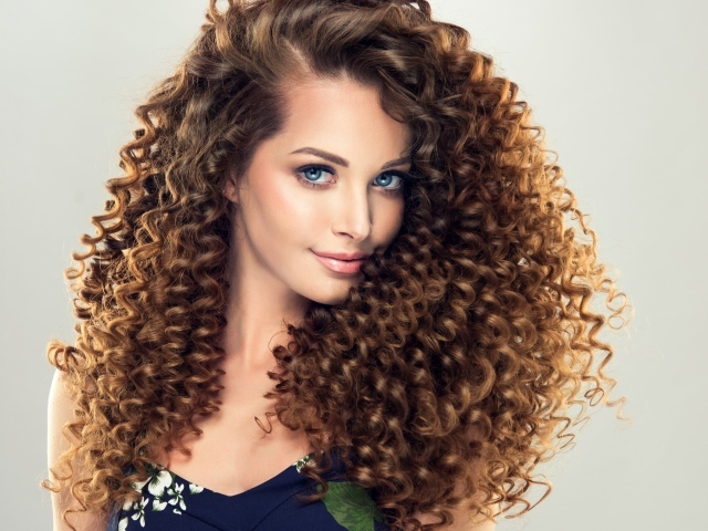 Красивая девушка с длинными волнистыми волосами на сером фоне