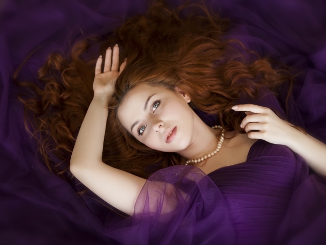 Красивая рыжеволосая девушка в лежит в фиолетовом платье