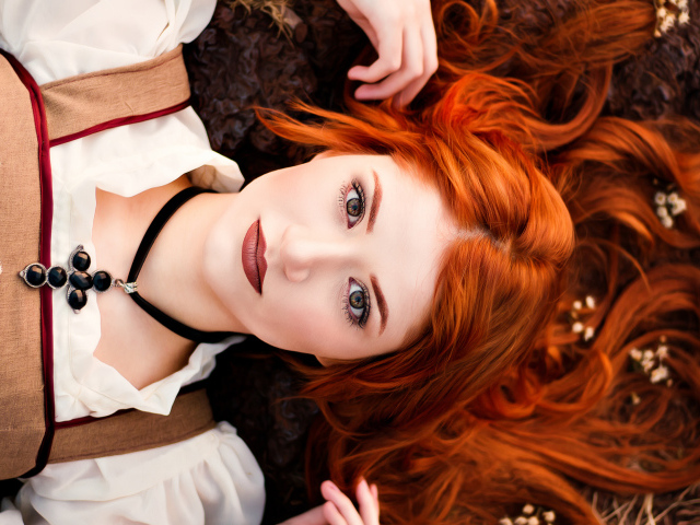 Красивая рыжеволосая девушка лежит на земле 