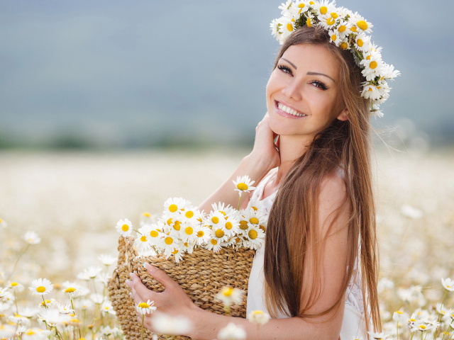 Красивая улыбающаяся девушка на поле с корзиной ромашек