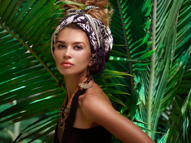 Красивая женщина в тюрбане с украшениями среди зеленых пальмовых листьев