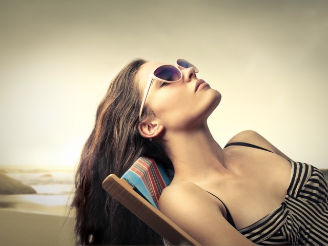 Красивая молодая девушка в очках лежит на шезлонге