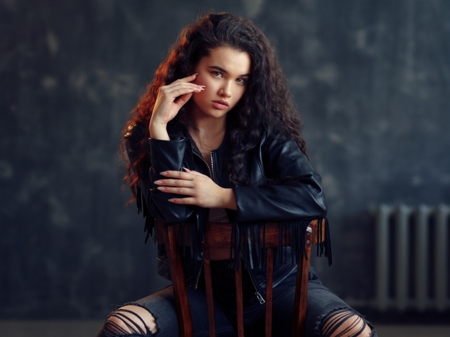 Модная красивая девушка в черное кожаной куртке сидит на стуле