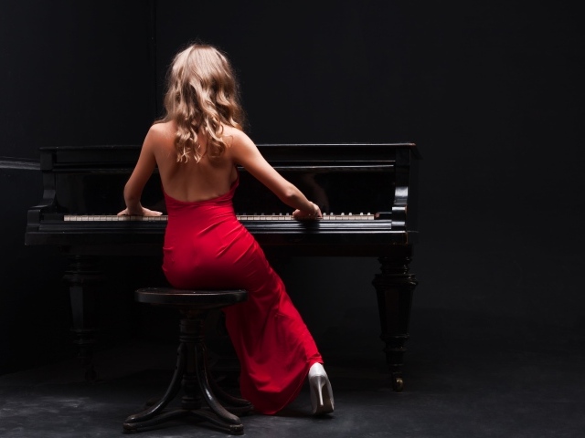 Молодая девушка в красном платье играет на пианино