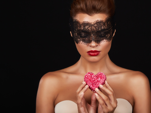 Молодая девушка в черной маске с красным сердцем в руках