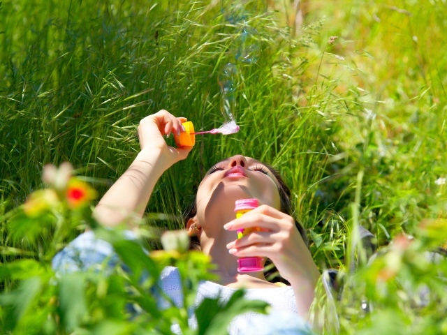 Молодая девушка лежит на зеленой траве с мыльными пузырями