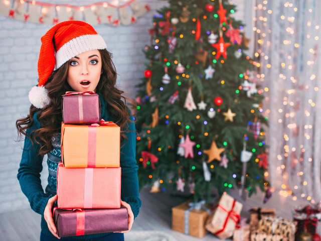 Удивленная девушка с подарками у новогодней елки 