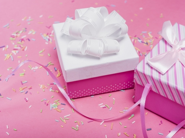 Две подарочные коробки с бантами на розовом фоне