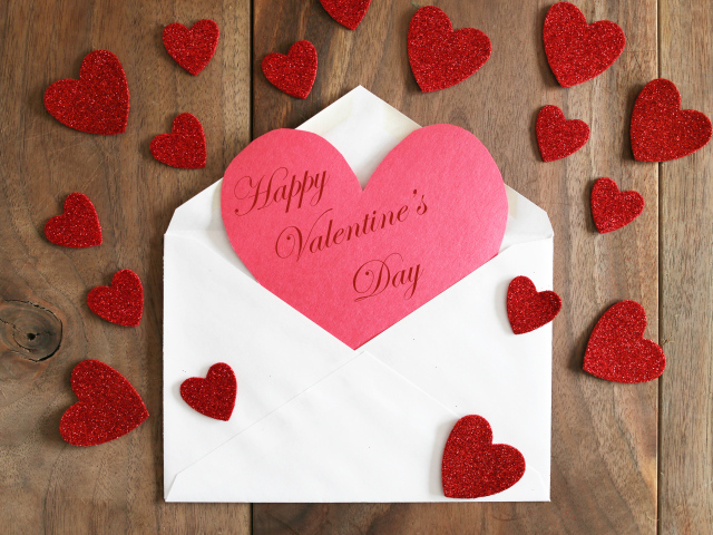 Белый конверт с валентинкой на деревянном столе с красными сердечками на 14 февраля