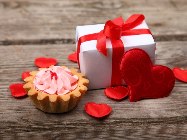 Подарок с красными сердечками и пирожным на столе