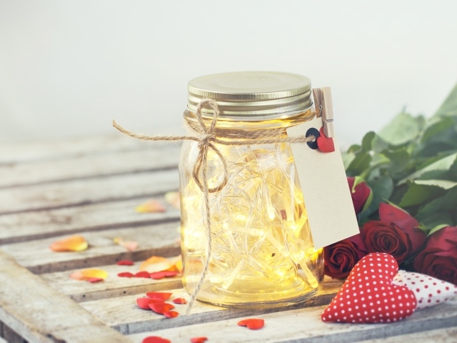 Стеклянная банка с гирляндой на столе с букетом роз и сердечками