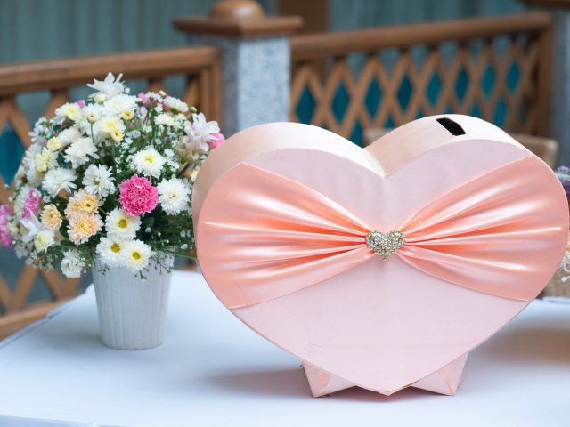 Большая розовая коробка в форме сердца на столе с букетом хризантем