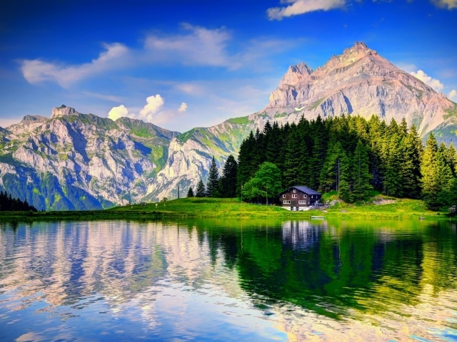 Лес и горы отражаются в озере под красивым голубым небом с белыми облаками