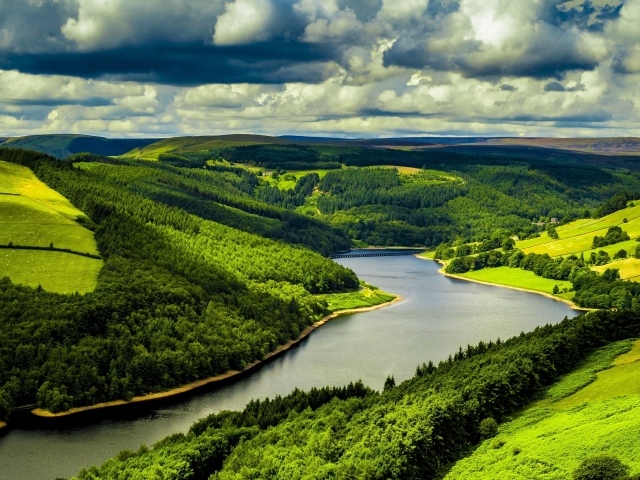 Зеленые холмы у реки под небом с густыми белыми облаками