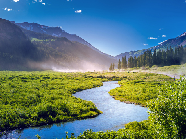 Речка на фоне покрытых зеленью гор под голубым небом