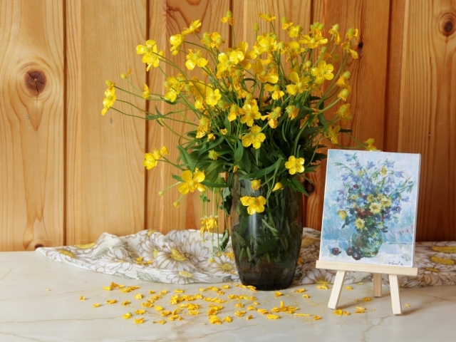 Букет желтых полевых лютиков в стеклянной вазе на столе с картиной
