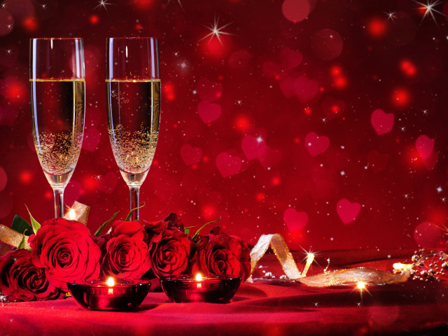 Букет роз и два фужера шампанского с зажженными свечами на красном фоне