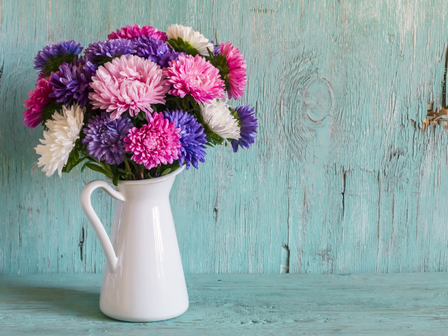 Разноцветные астры в вазе на деревянном фоне