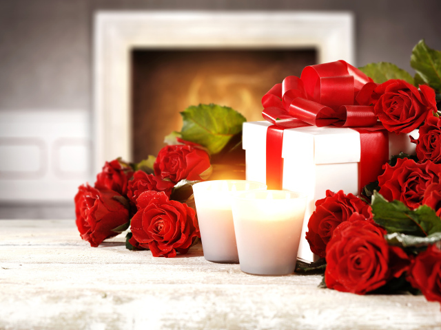 Красные розы с подарком и двумя зажженными свечами на столе