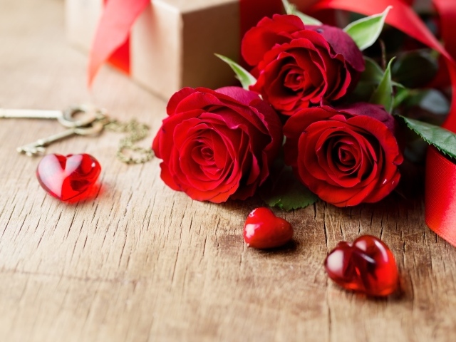 Три красных розы на деревянном столе с красными сердечками