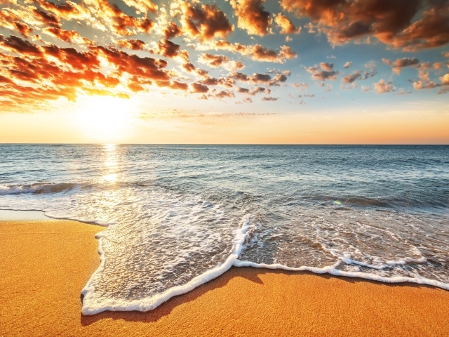 Морская волна омывает песок на берегу под красивым небом