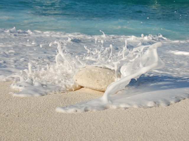 Белые морские волны бьются об камень на желтом песке