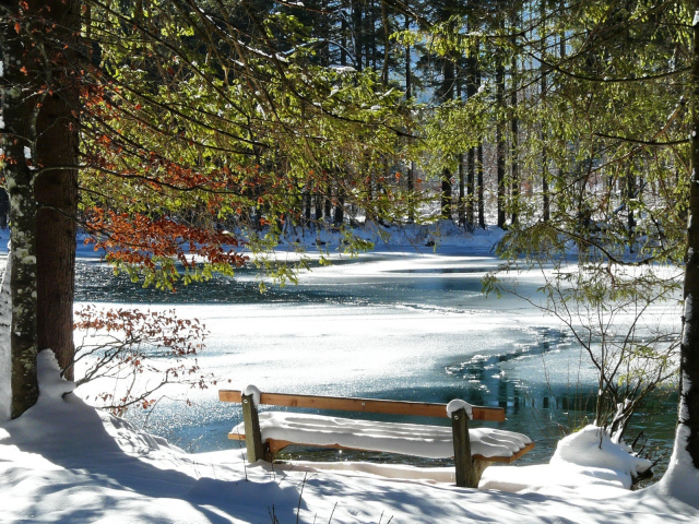Скамейка в парке у покрытого льдом тающего озера весной