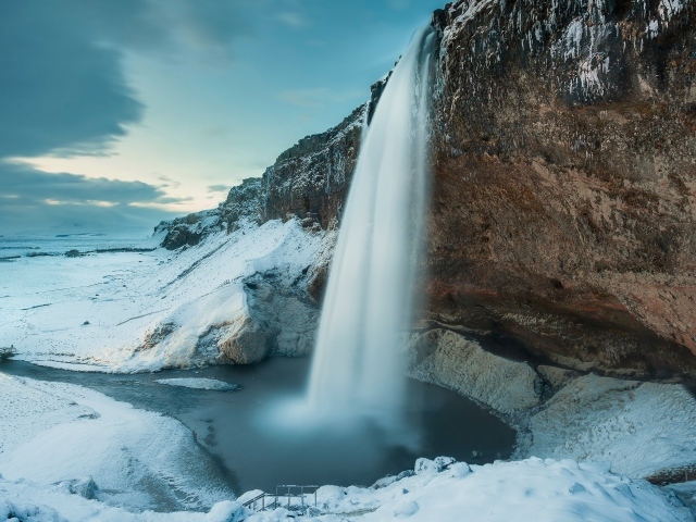 Водопад стекает с утеса на фоне заснеженной природы, Исландия