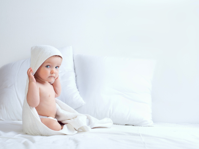 Грудной ребенок сидит на кровати с подушками