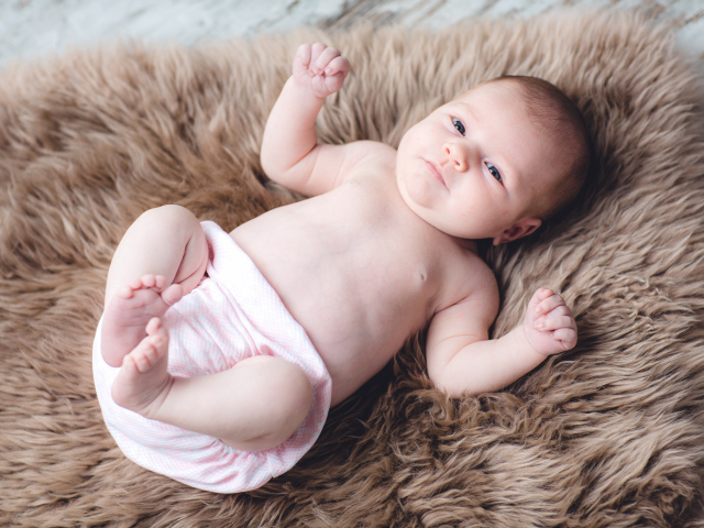 Грудной ребенок лежит на меховом покрывале