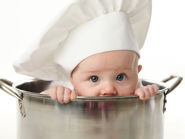 Грудной ребенок в шапке повара сидит в большой кастрюле