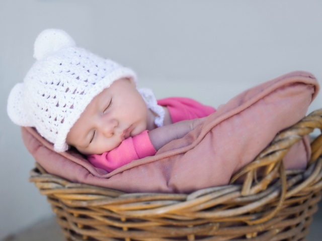 Маленький ребенок в белой шапке спит в корзине