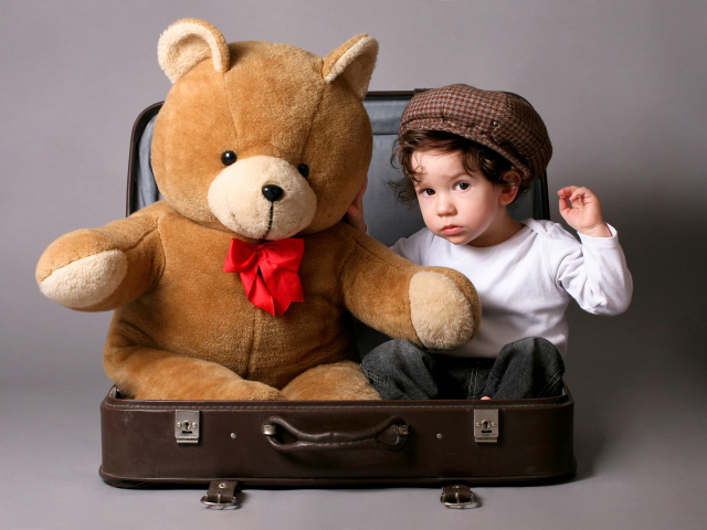 Маленький мальчик сидит в чемодане с плюшевым мишкой 