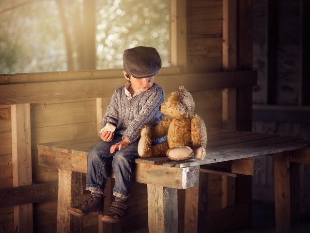 Маленький мальчик сидит на деревянном столе с медвежонком Тедди