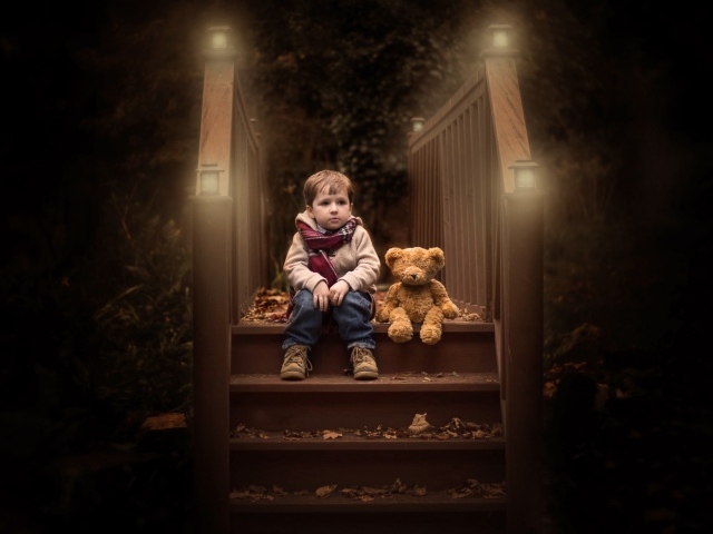 Маленький мальчик сидит с игрушечным мишкой на ступеньках