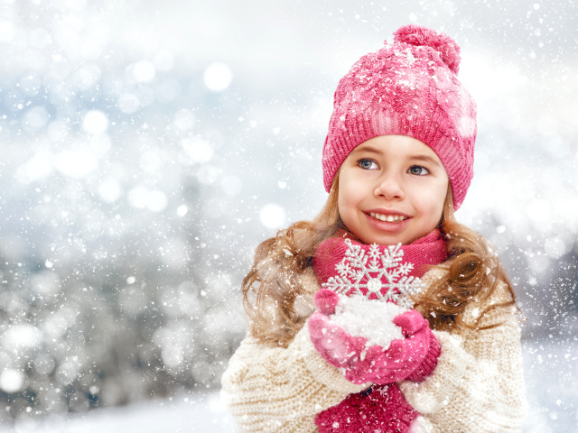 Маленькая девочка в зимней одежде держит снег в руках