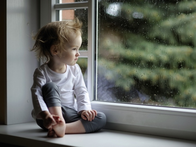 Маленькая девочка сидит на подоконнике у окна