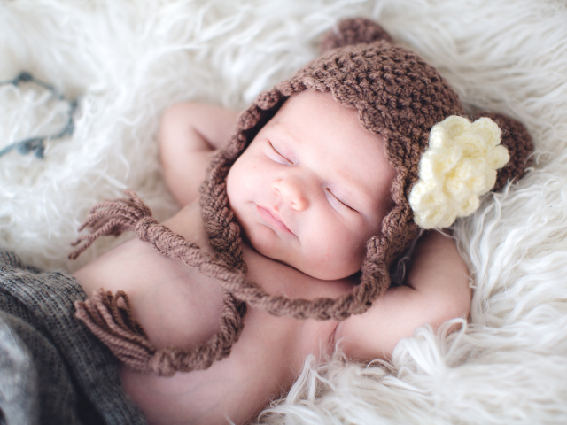Спящий грудной ребенок в коричневой вязаной шапке с белым цветком