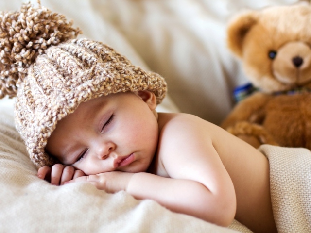 Спящий грудной ребенок в шапке с плюшевым мишкой