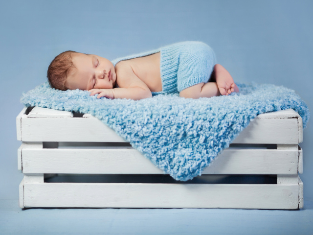 Маленький грудной ребенок спит на синем покрывале на деревянном ящике