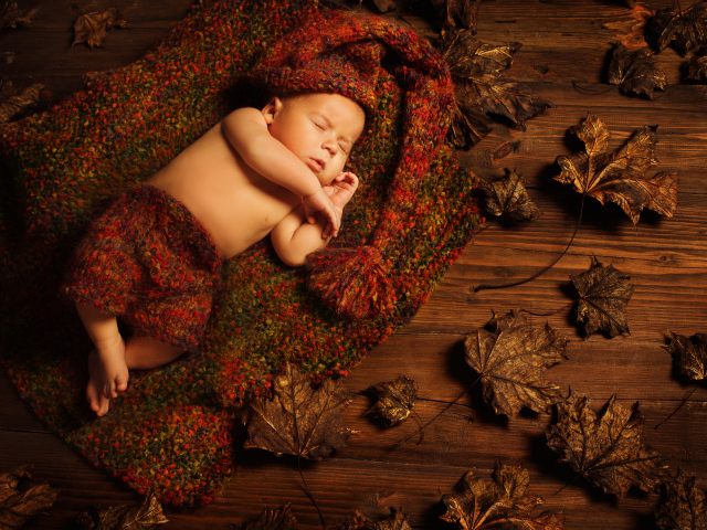 Маленький ребенок спит в вязаном костюме на полу с сухими листьями
