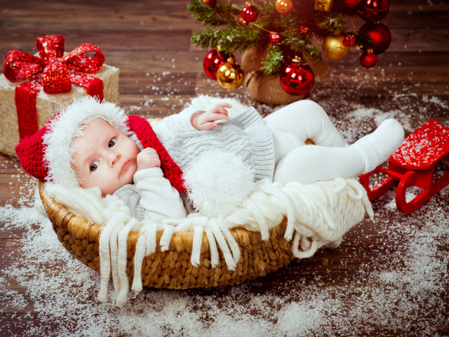 Младенец в корзине в новогоднем костюме под елкой с подарками