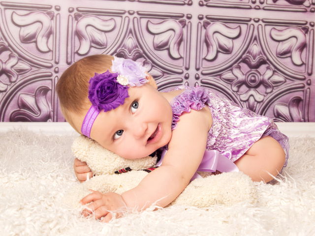 Красивая маленькая девочка в фиолетовом костюме с плюшевым мишкой