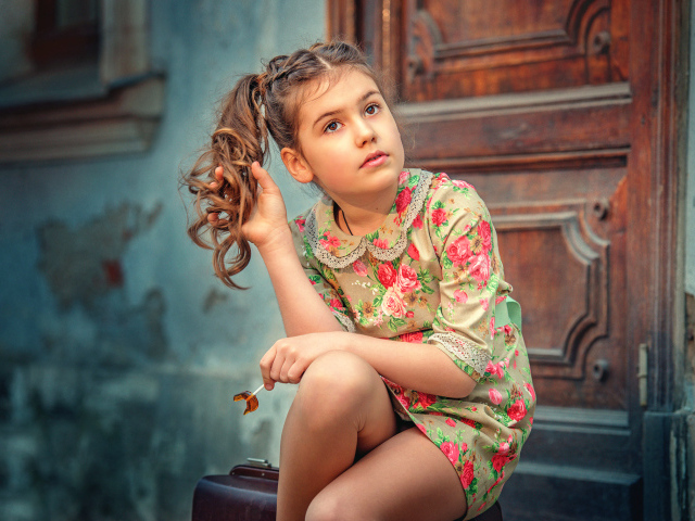 Кареглазая девочка в цветастом платье сидит на пороге