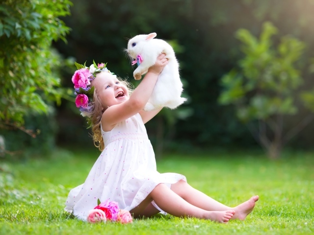 Радостная маленькая девочка в белом платье с кроликом в руках