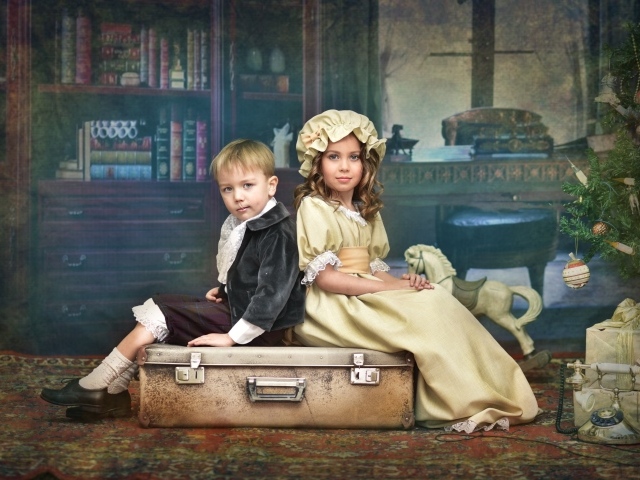 Маленькие мальчик и девочка в винтажных костюмах сидят на чемодане