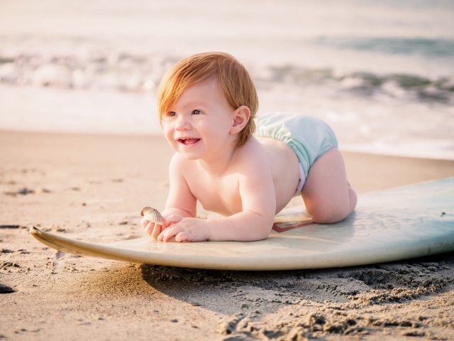 Маленький мальчик на доске для серфинга на пляже